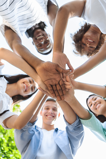 Friends Unity. Low Angle Portrait Of Happy Teenage People Stacking Hands Together And Smiling At Camera, Showing Teamwork And Cooperation