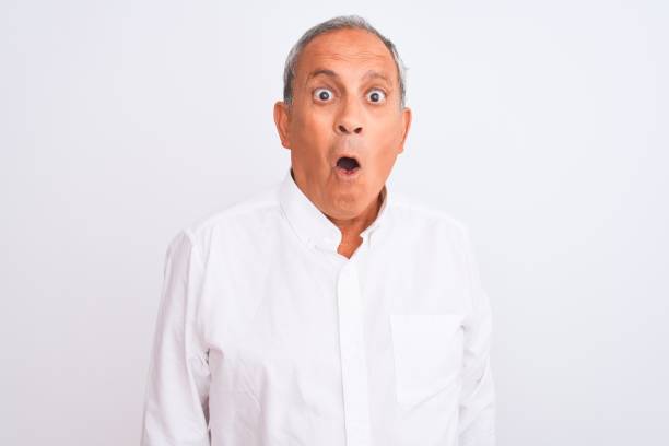 Senior grey-haired man wearing elegant shirt standing over isolated white background afraid and shocked with surprise expression, fear and excited face.