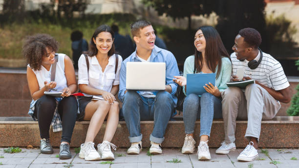 istock Joyful University Students Sitting At Campus With Laptop And Laughing Together 1212744149