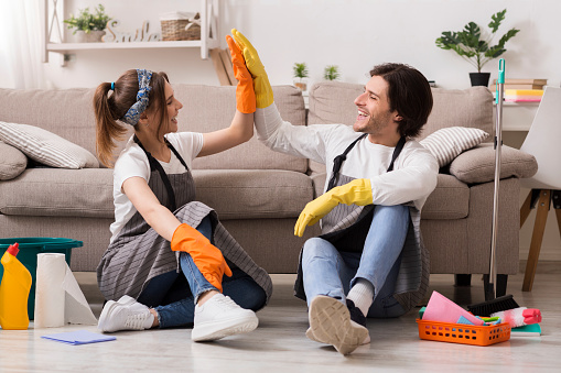 Housekeeping And Cleaning Service Concept. Happy Couple Giving High Five To Each Other After Spring-Clean In Apartment
