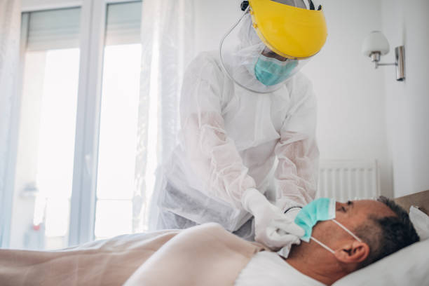 medico che applica la maschera facciale a un uomo anziano che si trova nel letto d'ospedale a causa dell'infezione da coronavirus - protective suit foto e immagini stock