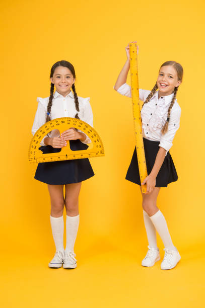 istock happy math. stem disciplines. back to school. Maths and geometry. Kids in uniform at yellow wall. friendship and sisterhood. happy small girls study mathematics. students use protractor ruler 1212745959