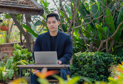 A handsome young businessman working on a desk with a laptop in his garden.