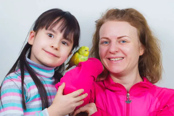 Photo of mother and daughter communicate with their tame yellow parrot.