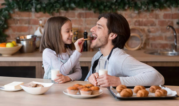 niña cariñosa alimentando a su padre con galletas en la cocina - domestic kitchen father eating child fotografías e imágenes de stock