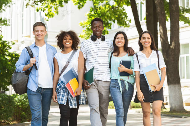 cheerful college students walking out of campus together, posing outdoors - adult education full length book imagens e fotografias de stock