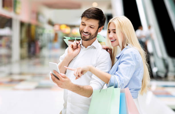 istock Spouses Using Smartphone Searching Sales And Offers Standing In Mall 1212748214
