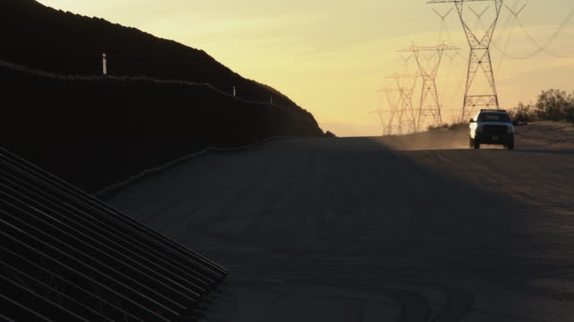 A Sunset View Of The International Border Wall, An Agent Patrolling,California, United States Side