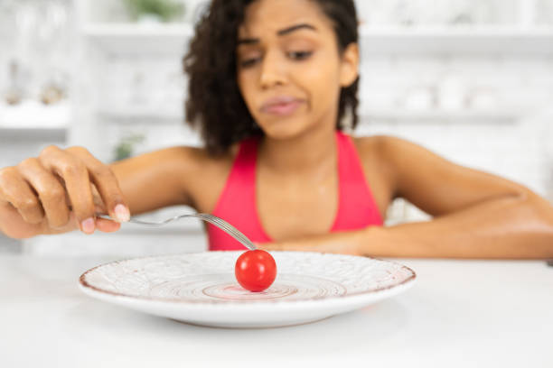 istock Unhappy afro woman looking at tiny tomato on a plate 1212748864
