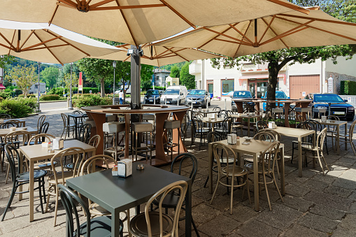 Street restaurant with tables and chairs under umbrellas at hotel in Italy. Design of Sidewalk cafe outdoor. Italian Terrace or veranda of cafe ready for breakfast or lunch. Lifestyle and food.