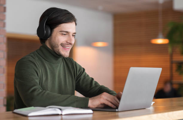 istock Young positive man in wireless headphones studying online on laptop 1212750310