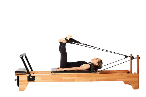 Young woman exercising on a Pilates machine on white background