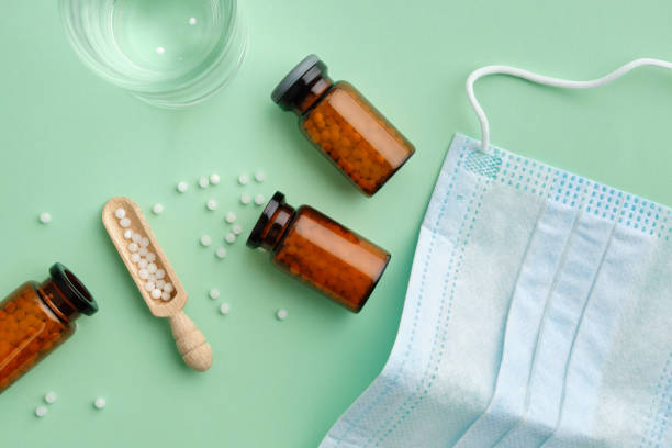istock Bottles of homeopathic granules, water glass for preparation of medicinal solution, protective medical mask. Top view. 1212750687