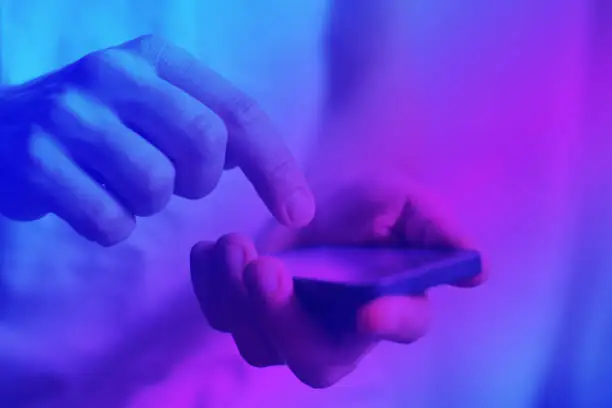 Photo of hands using smartphone closeup in neon light