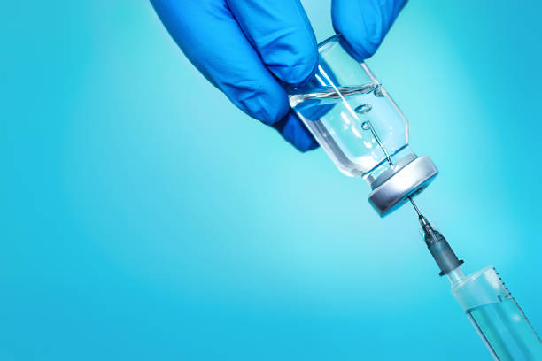 uma garrafa com vacina e seringa em um fundo azul. o conceito de medicina, saúde e ciência - injeção insulina luva - fotografias e filmes do acervo