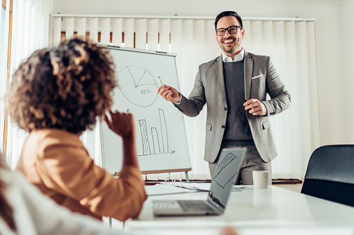 Cheerful young businessman wearing grey suit and eyeglasses talking to colleagues at the meeting during business presentation