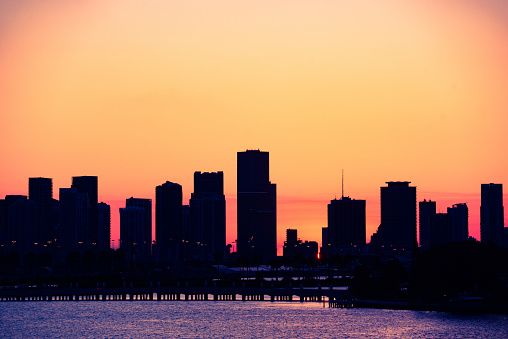 This is a color photograph of a orange sunset sky creating a silhouette of the Downtown Miami buildings along Biscayne Boulevard seen behind the bridge to Star Island in Miami Beach, Florida.