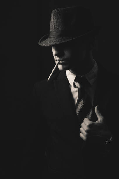 Retro man in hat wears suit and tie Retro man in hat wears suit and tie with cigarette, black and white. Noir style. 1930s style men image created 1920s old fashioned stock pictures, royalty-free photos & images