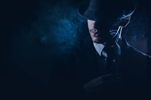 Retro man in smoke wears suit, tie and hat Retro man in smoke with hat, suit and tie smoking cigarette, blue light. Noir style. 1930s style men image created 1920s old fashioned stock pictures, royalty-free photos & images