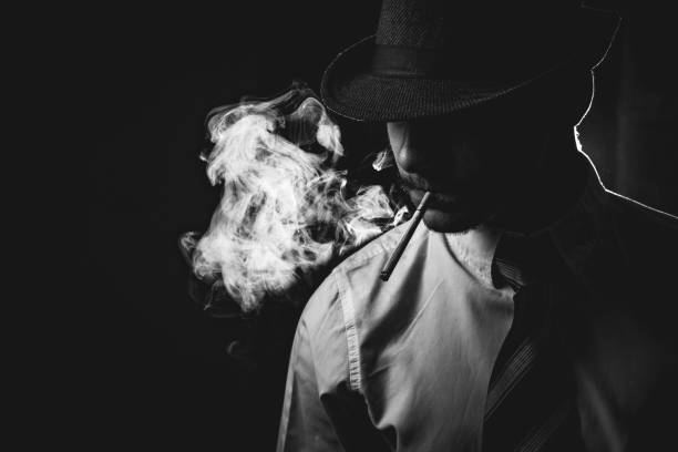 Retro man in smoke wears tie and hat Retro man in smoke with hat, shirt and tie, smoking cigarette, black and white. Noir style. organized crime photos stock pictures, royalty-free photos & images
