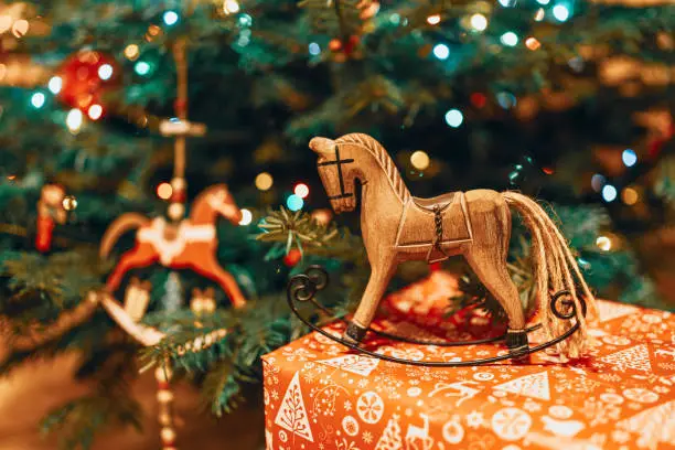 Christmas hobbyhorse made of wood on a present near a Christmas tree. Suitable for horse riding theme greetings, postcards, backgrounds and social media posts just in time for Christmas.