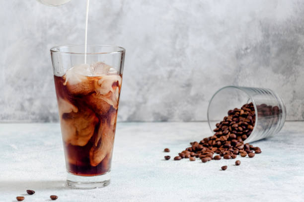 istock Milk Being Poured into Iced Coffee in Tall Glass on Light Grey Background. Concept Refreshing Summer Drink 1212759457