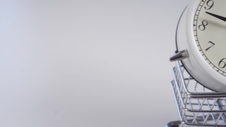 Decorative supermarket trolley with an analog white alarm clock is rolling on a light table