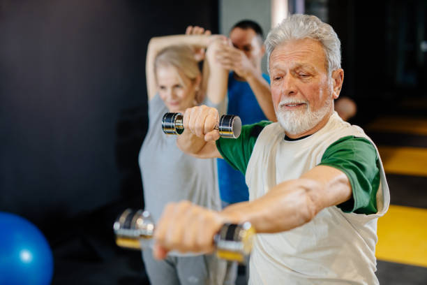 istock Senior couple exercising with personal trainer using dumbbells at the gym 1212764435