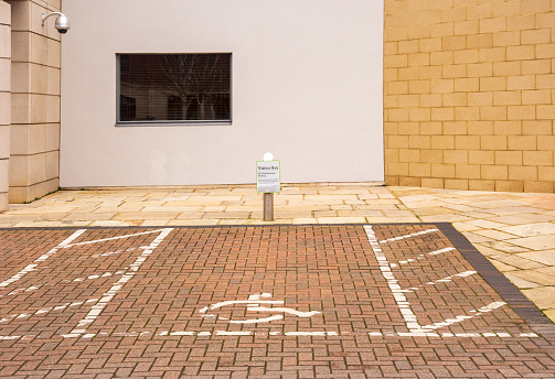 A visitor parking bay reserved for the disabled with wheelchair symbol and a post with sign outside an office building