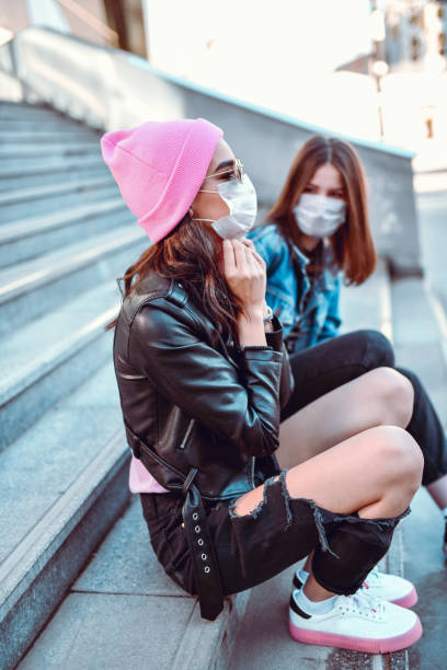 femmine sedute su scale con maschere protettive a causa della pandemia di coronavirus - rock staircases foto e immagini stock