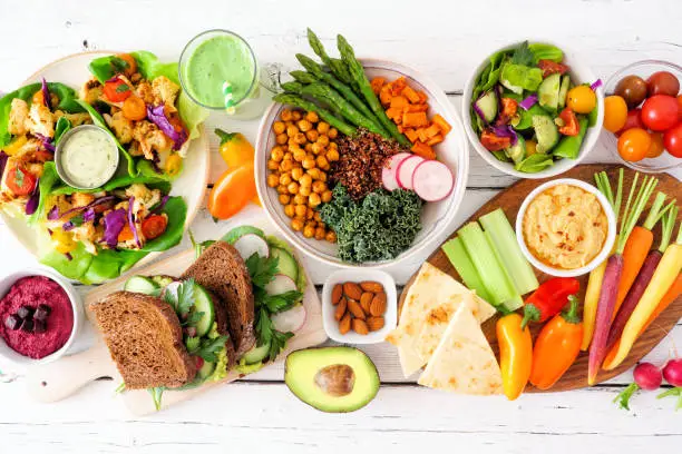 Photo of Healthy lunch table scene with nutritious lettuce wraps, Buddha bowl, vegetables, sandwiches, and salad, overhead view over white wood