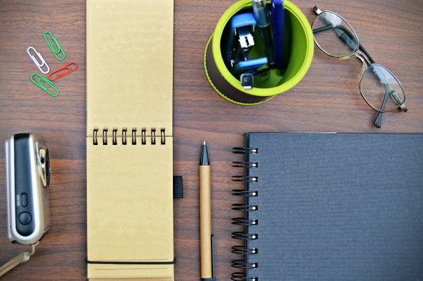 istock Stationery, like pen holder, diary, staple placed aesthetically with spectacles and camera over a wooden dark brown color horizontal background. 1212770575