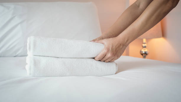 istock Close-up of hands putting stack of fresh white bath towels on the bed sheet. 1212770596