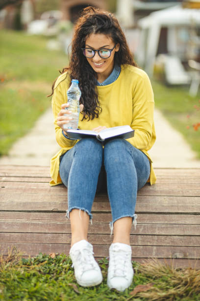 本と飲料水で自然の中でリラックスした若い女性 - balance book university glasses ストックフォトと画像