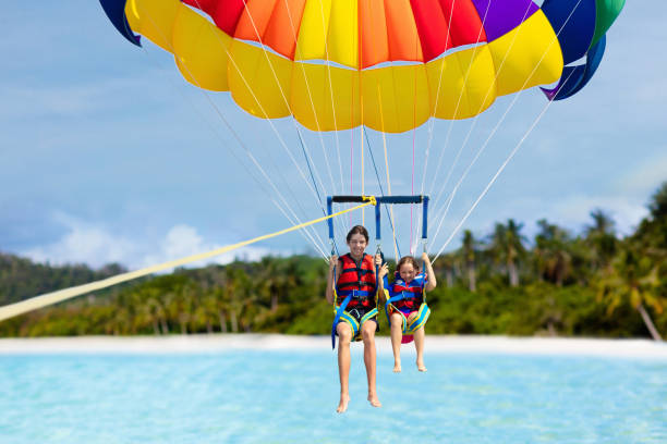 Kids parasailing. Water sport on summer vacation. Kids parasailing. Water sport on summer vacation. Brother and sister flying in tropical ocean resort. Sea and beach fun. Rainbow parachute. Teenage boy and little girl fly. parasailing stock pictures, royalty-free photos & images