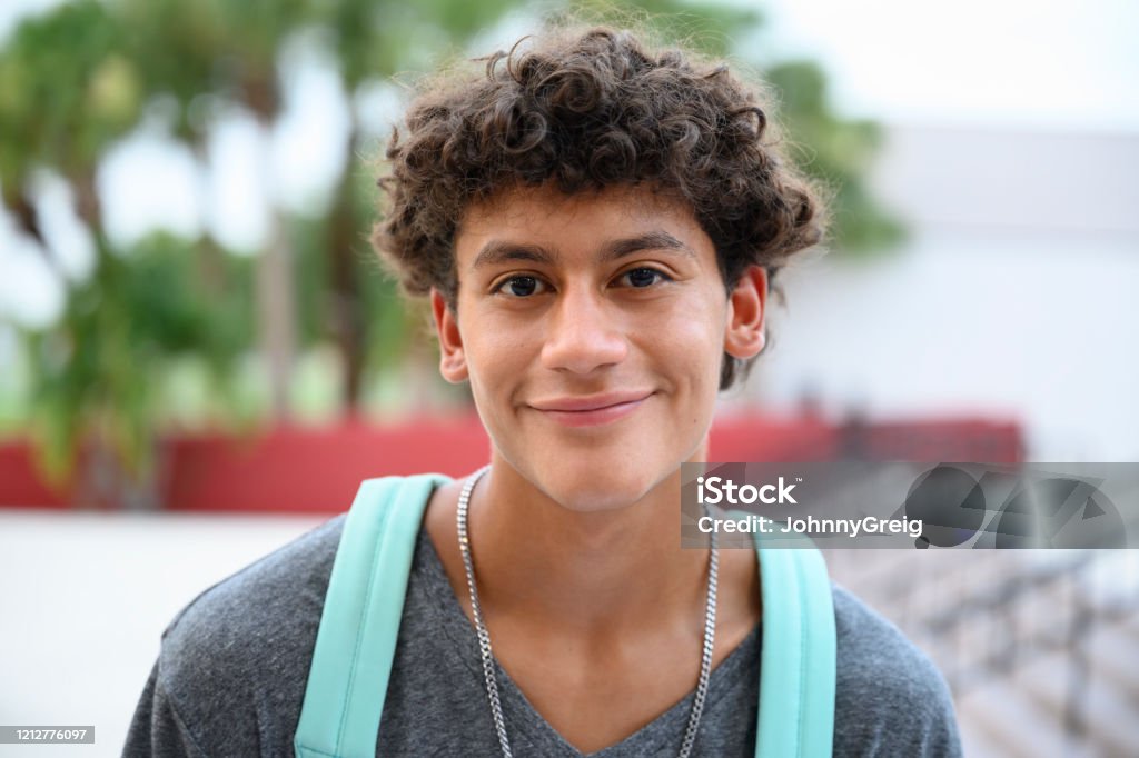 Portrait of contented male Hispanic teenager Headshot of smiling Hispanic teenage boy standing outside school with backpack and looking at camera before going to class. Teenager Stock Photo