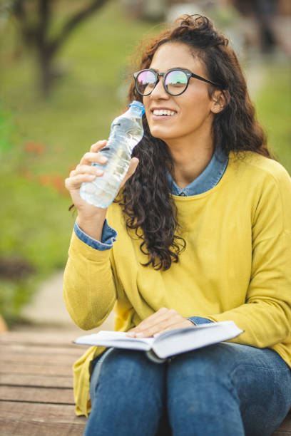 本と飲料水で自然の中でリラックスした若い女性 - balance book university glasses ストックフォトと画像