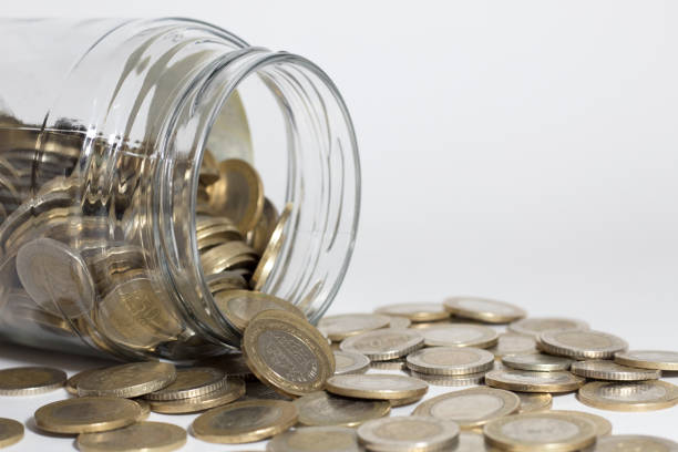 Euro coins spilling out a money jar shot on white background.Selective focus.  Predominant colors are bronze and white. High resolution 42Mp studio digital capture taken with Sony A7rII and Sony FE 90mm f2.8 macro G OSS lens