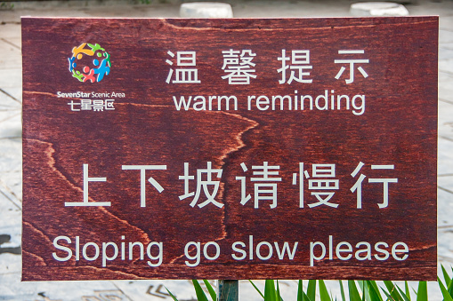 Guilin, China - May 11, 2010: Seven Star Park. White on brown warning sign about going slow on slope with funny spelling error in English.