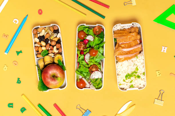 School lunch and stationery. School lunch and stationery. Lunch boxes with chicken, rice, salad, fruits and nuts on an orange background, top view. Healthy balanced food for children in lunchboxes, flat lay. packed lunch photos stock pictures, royalty-free photos & images