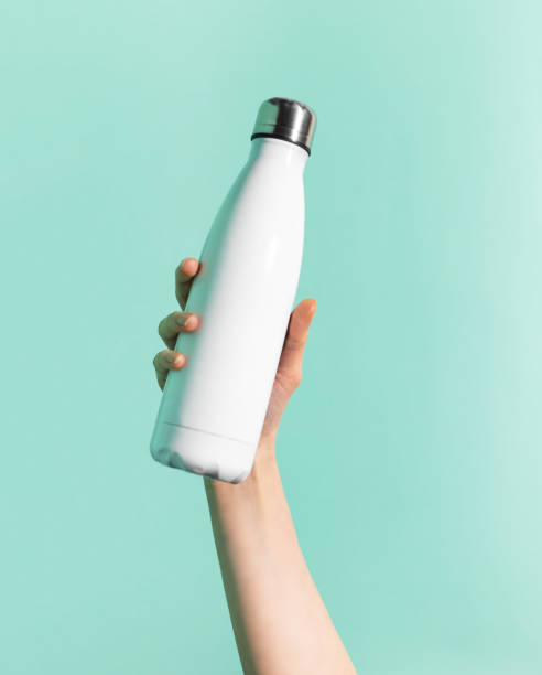 Close-up of female hand holding white reusable steel stainless thermo water bottle isolated on background of cyan, aqua menthe color. Plastic free. Close-up of female hand holding white reusable steel stainless thermo water bottle isolated on background of cyan, aqua menthe color. Plastic free. plastic free photos stock pictures, royalty-free photos & images