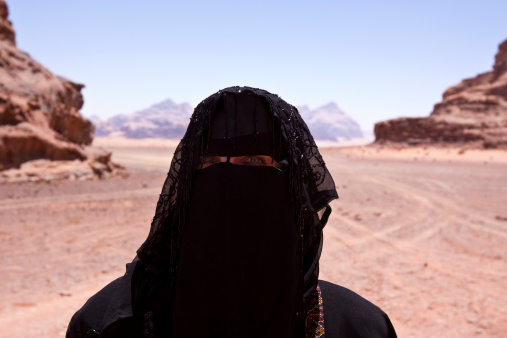 Bedouin woman dressed in Traditional burka standing alone in the the desert of jordan called 