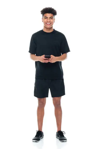 Photo of African-american ethnicity male standing in front of white background wearing sports shoe and using mobile phone