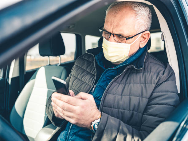 istock COVID-19, Mature man wearing on disposable face mask using mobile phone 1212801575