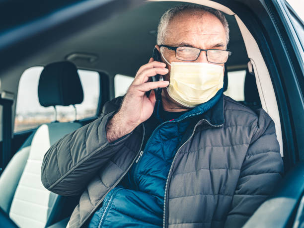 istock COVID-19, Mature man wearing on disposable face mask using mobile phone 1212801992