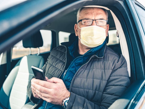 istock COVID-19, Mature man wearing on disposable face mask using mobile phone 1212801995