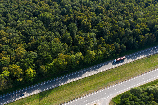 The truck is in a hurry to deliver the cargo, driving along a straight highway laid through the forest. Top view, shot on a drone.