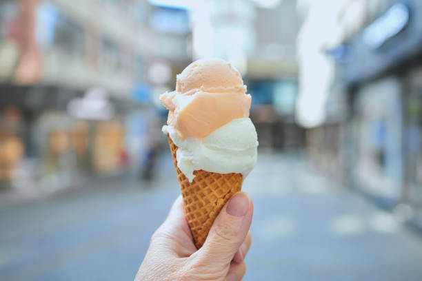 ice cream cone with two balls of ice cream in front of shops in a city center stock photo