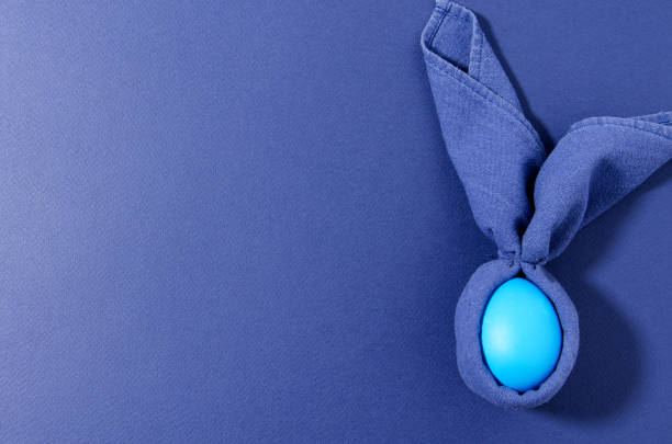 istock Creative easter bunny blue egg wrapped in a blue napkin and lies on a blue background. Minimalization trend monochrome, horizontal background 1212810561