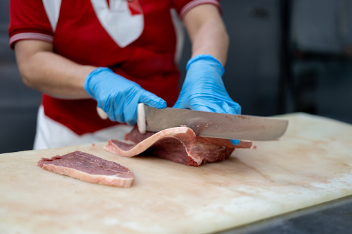 Unrecognizable female butcher cutting a slice of meat with a sharp knife